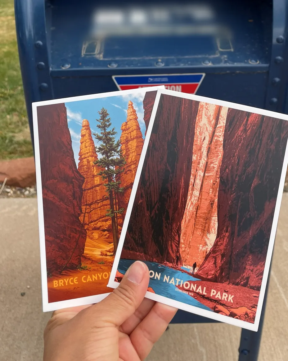 Two national park postcards, Bryce Canyon and Zion, held up at a blue mailbox.