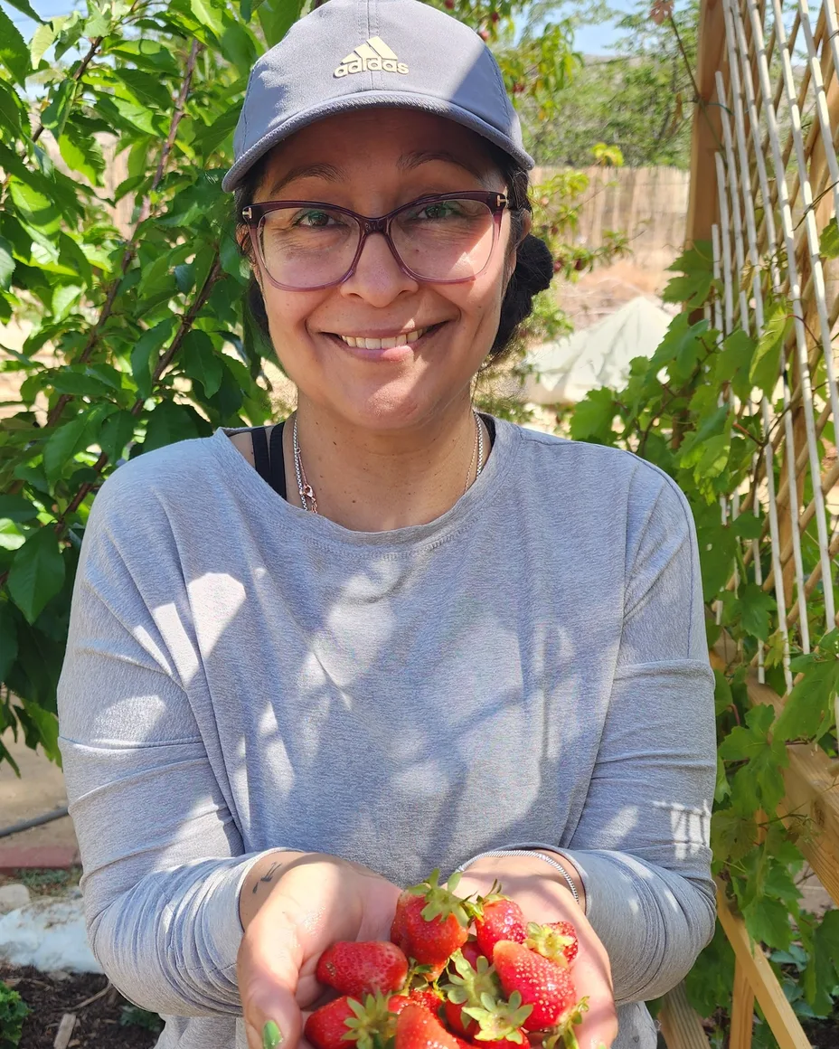 Nikki in her garden, holding out a handful of strawberries.