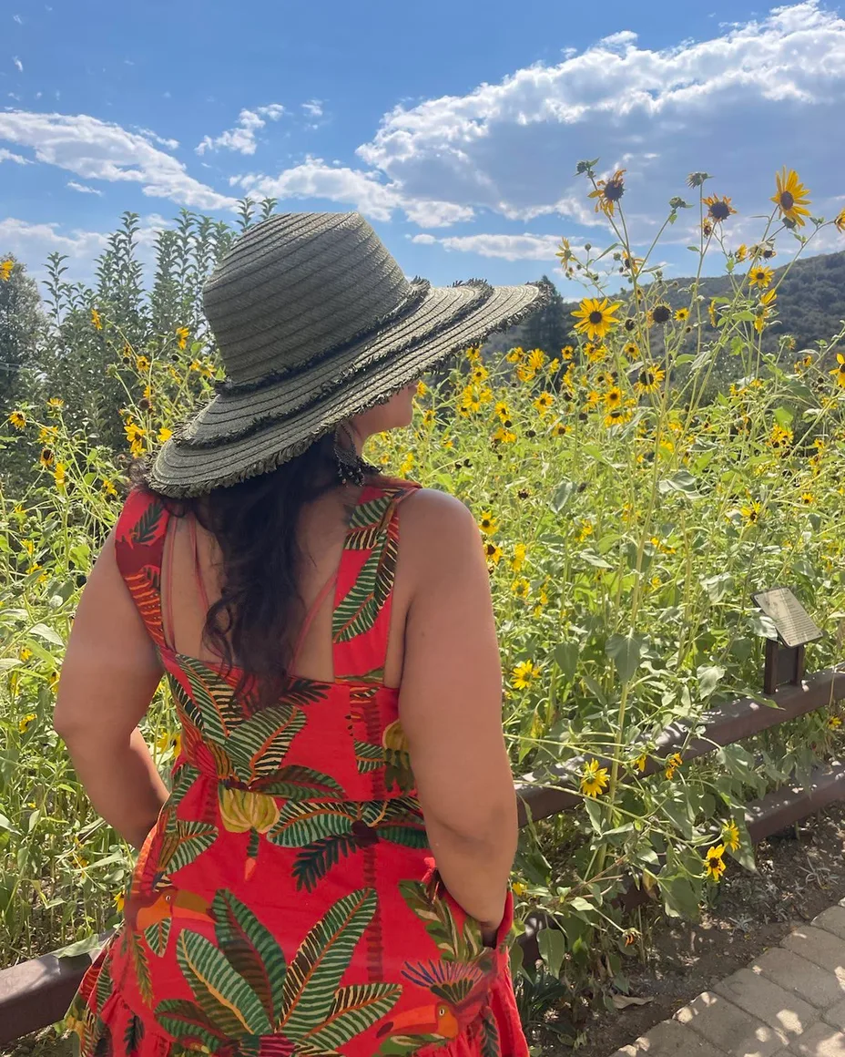 Nikki from behind in a straw sun hat, walking into a field of yellow flowers.