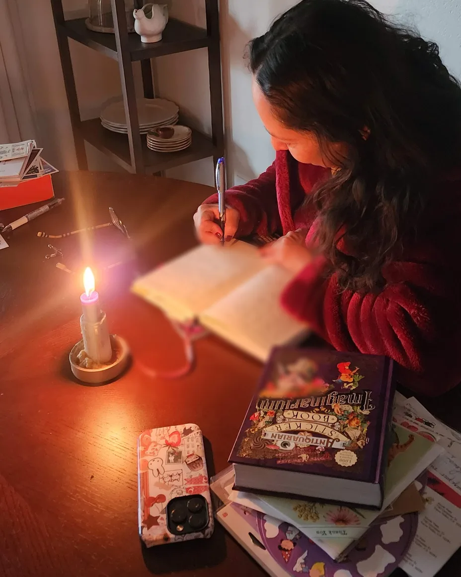 Nikki at her table by candlelight, writing in her notebook with a pen.